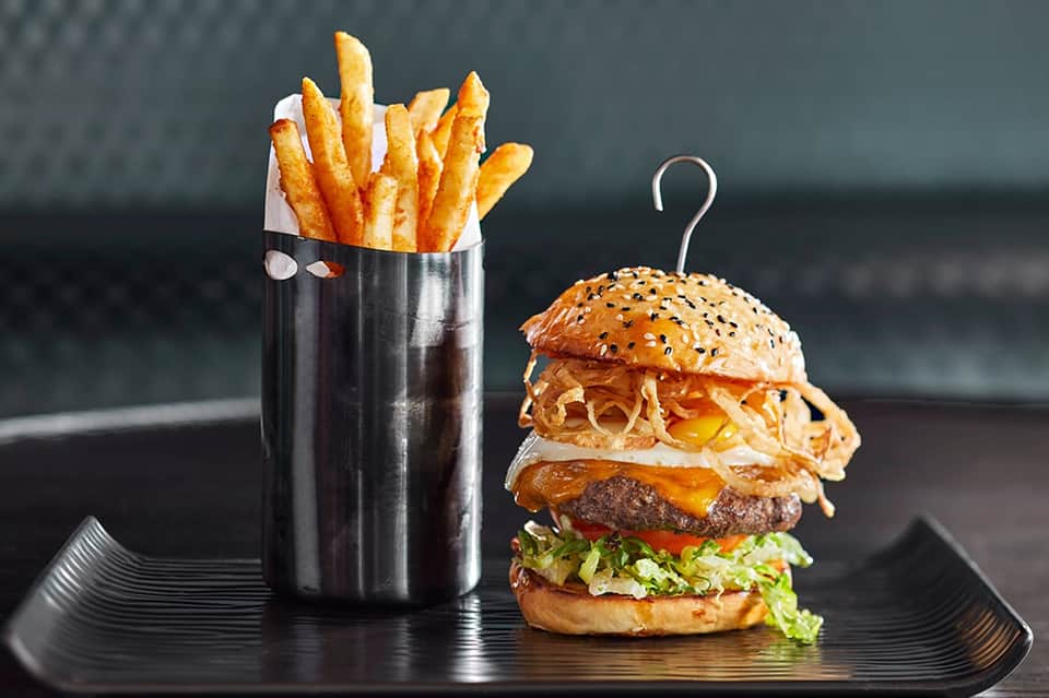 Gourmet burger with crispy fries in a metal cup on a black plate
