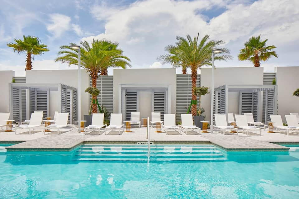 Contemporary pool deck with white loungers, palm trees, white cabanas, and turquoise water