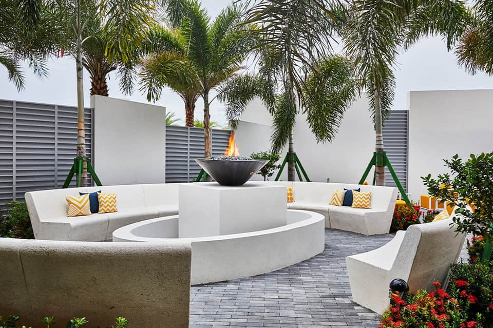 Resort fire pit lounge area with curved white seating, palm trees, and decorative pillows