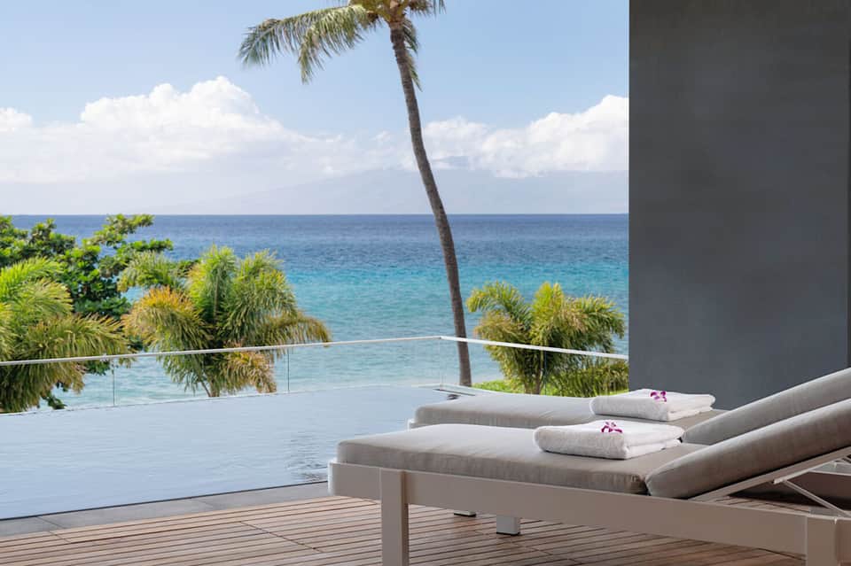 Luxury oceanfront terrace with loungers, towels, ocean view, and palm tree