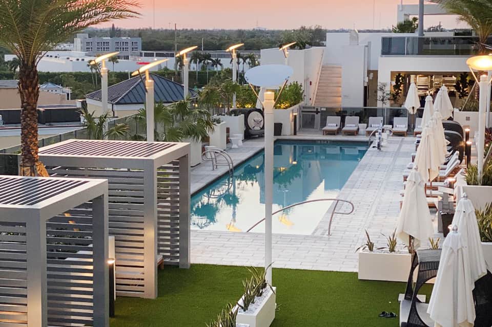 Elevated view of luxury rooftop pool at dusk with modern white loungers, heaters, and city skyline