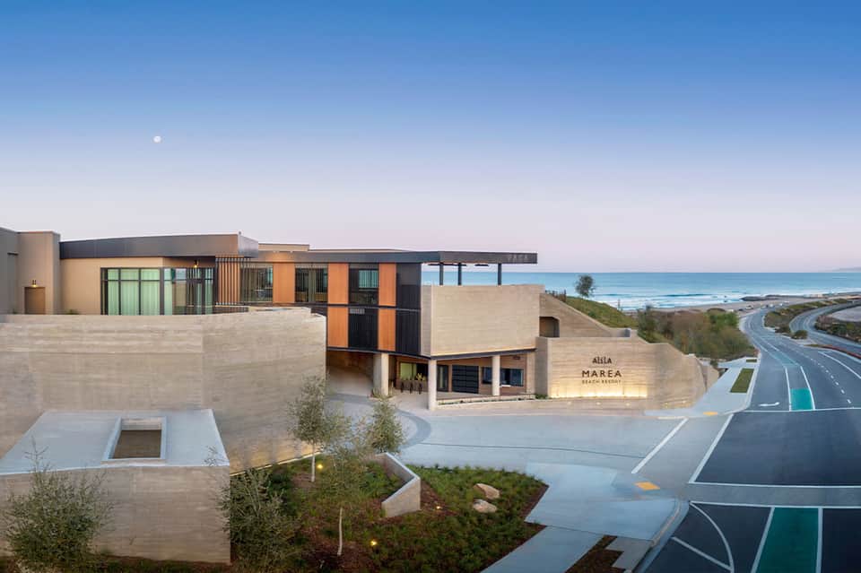 Modern beach resort building with beige stone, orange and black metal panels overlooking ocean and coastline