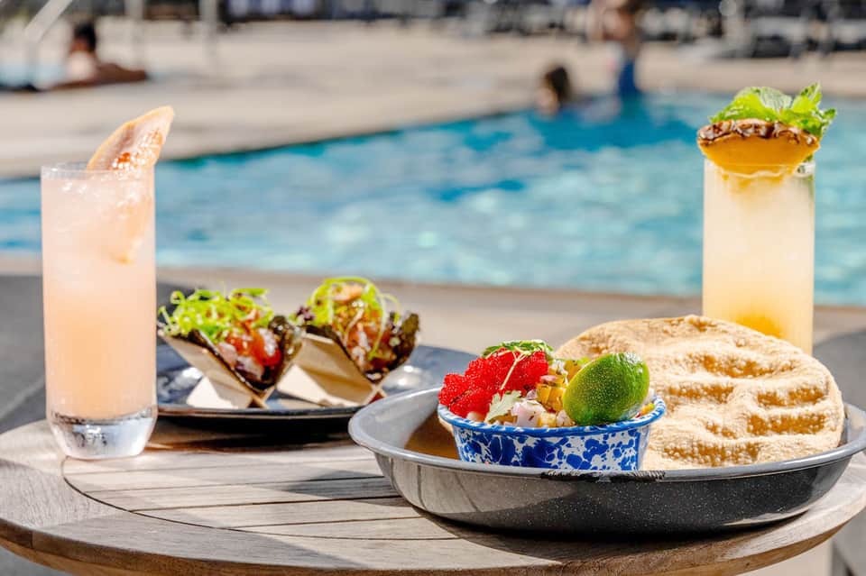 Cocktails and tropical appetizers on poolside table overlooking resort swimming pool