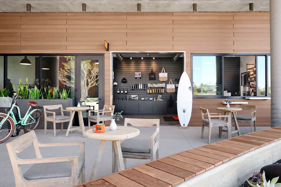 Modern beachfront resort exterior with wood facade, café seating, and surfboard display