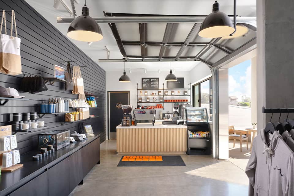 Modern coffee shop interior with black pendant lights, black shiplap walls, shelving displays, and glass garage doors