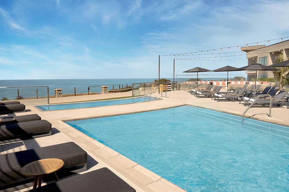 Elevated infinity pool deck overlooking ocean with lounge chairs, umbrellas, and contemporary architecture