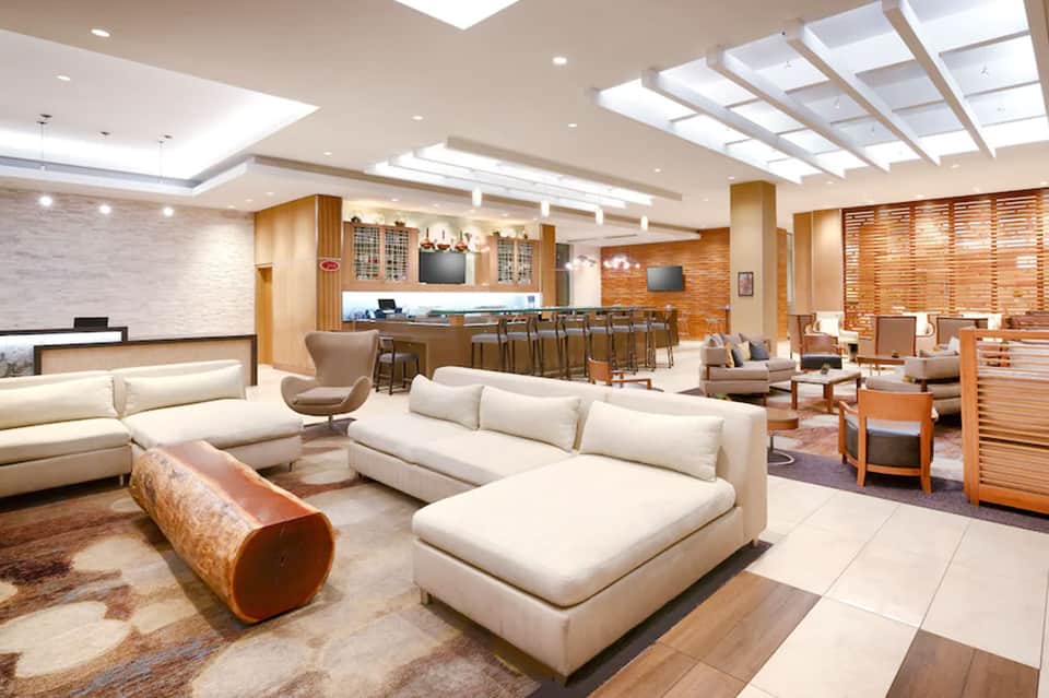 Modern hotel lobby lounge with cream sofas, bar seating, and skylight ceiling