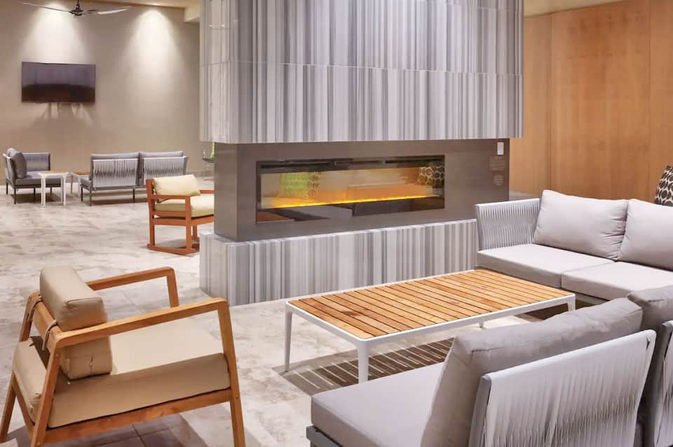 Contemporary hotel lounge with modern fireplace, wooden furniture, and light gray seating