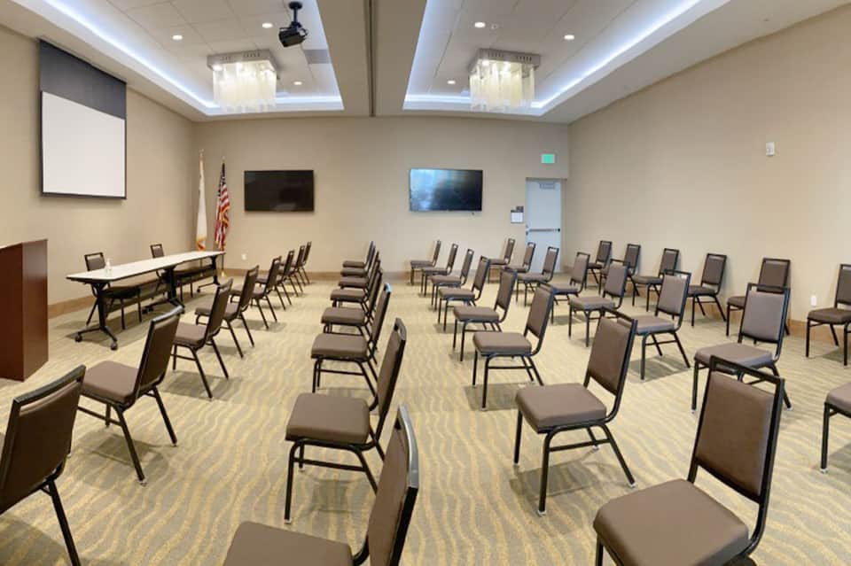 Conference room with rows of theater-style seating, projector screen, and podium