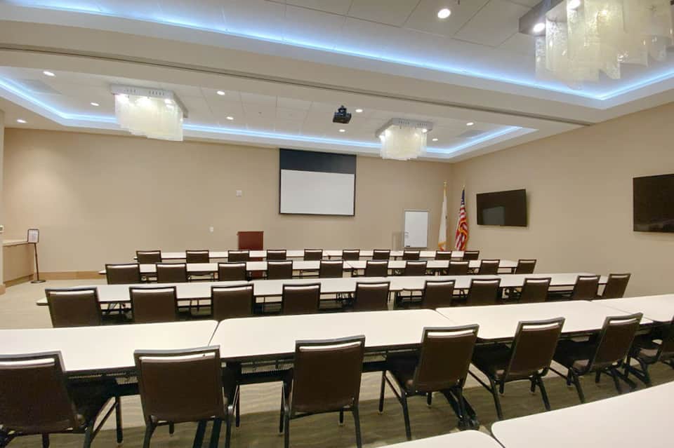 Empty hotel conference room with rows of brown chairs and projection screen setup