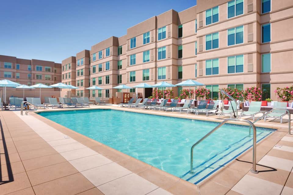 Resort pool with turquoise water, loungers, umbrellas, and multi-story hotel building