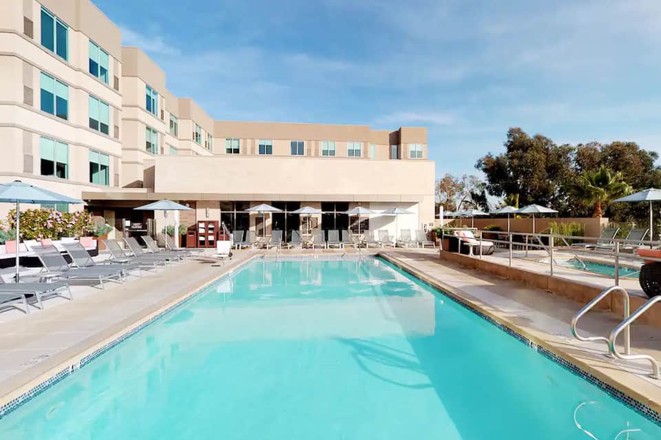 Hotel pool deck with turquoise water, white umbrellas, lounge chairs, and modern building facade