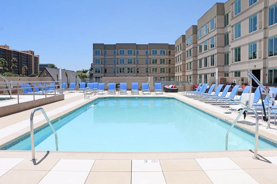 Outdoor swimming pool surrounded by blue loungers, brick buildings, and blue privacy screen