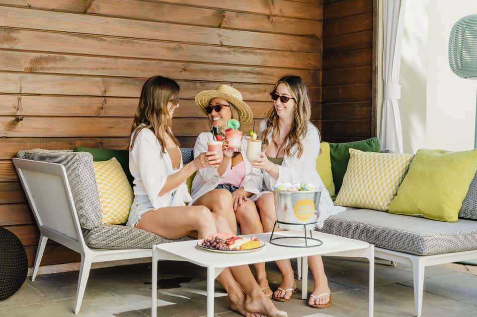 Three women relaxing on cushioned lounge furniture with drinks and fresh fruit platter