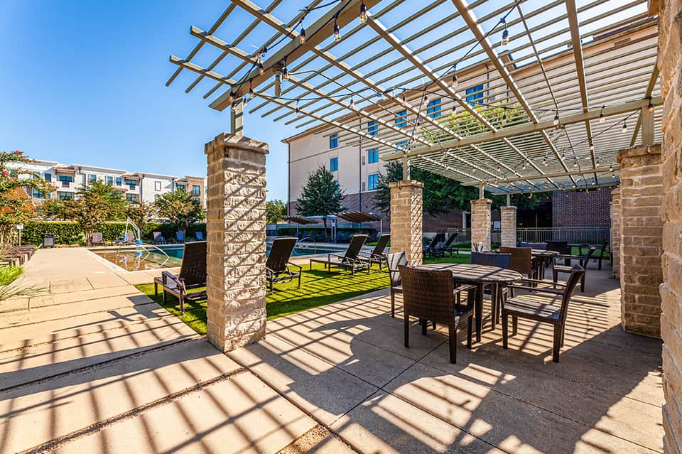 Outdoor patio with pergola, stone columns, and lounge seating overlooking manicured lawn