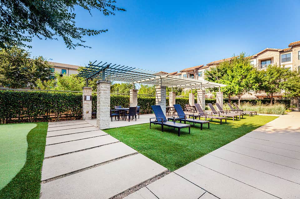 Modern resort courtyard with pergola structure, lounge chairs, lawn, and trees
