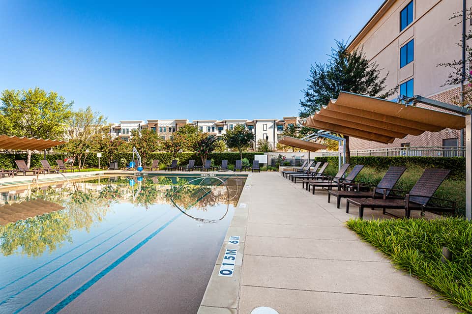 Resort lap pool with lane dividers, lounge chairs, wooden shade structures, and residential buildings