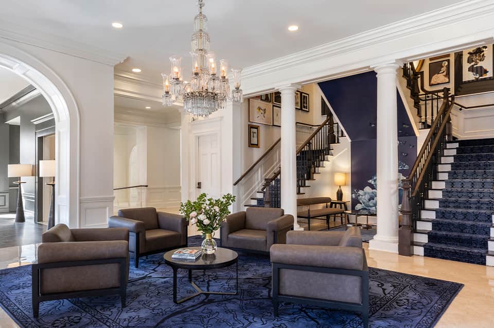 Elegant hotel lobby with crystal chandelier, neutral furniture, columns, and grand staircase