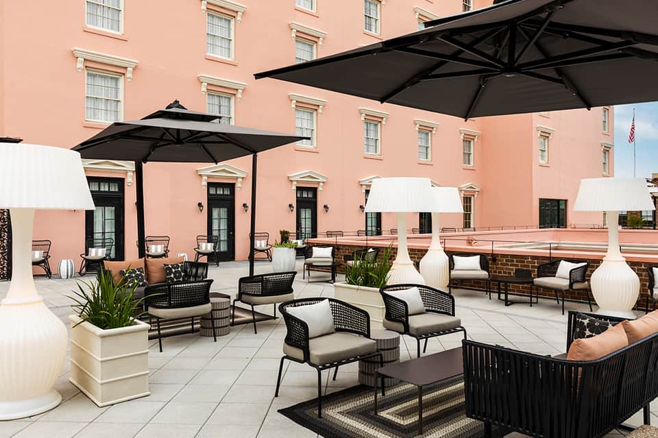 Elegant outdoor terrace on coral-colored building with black umbrellas, modern furniture, and landscape lighting