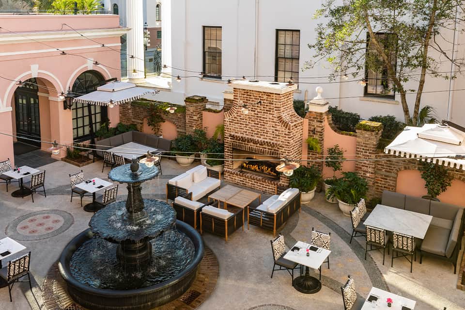 Courtyard seating area with fountain, brick walls, white umbrellas, and lounge furniture