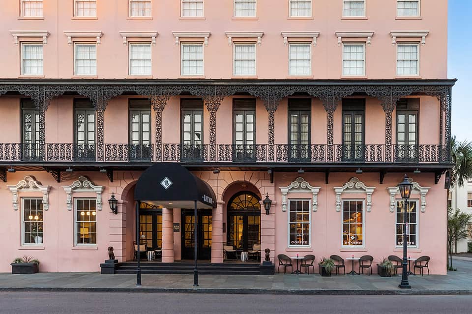 Pink colonial-style hotel building facade with ornate wrought-iron balcony and entrance