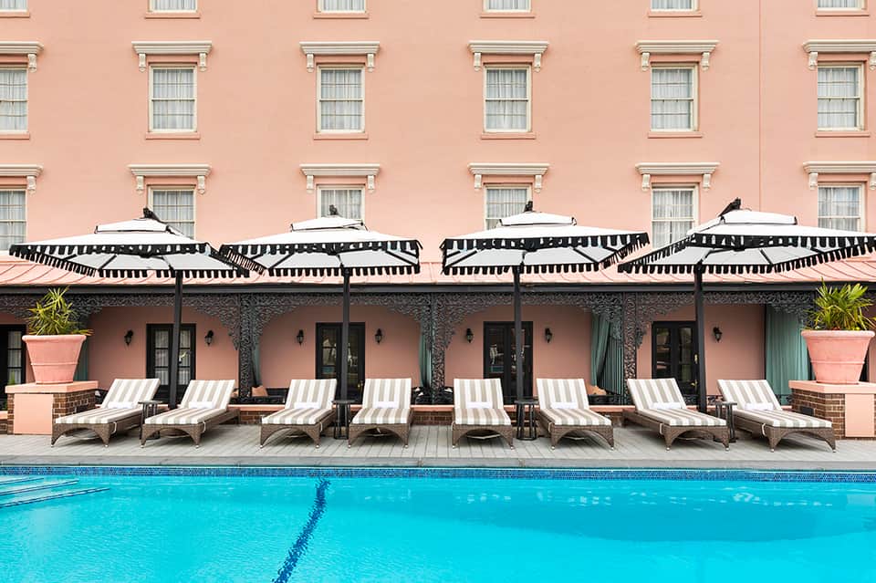 Classic hotel pool with striped umbrellas, pink building facade, and multiple lounge chairs
