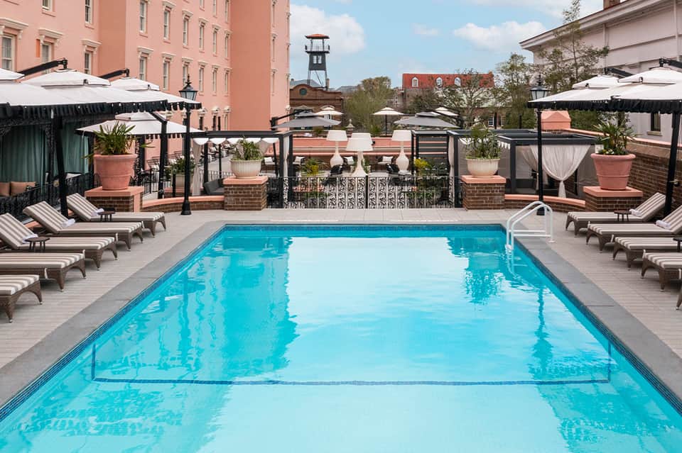 Rooftop swimming pool with loungers and black umbrellas surrounded by historic brick buildings