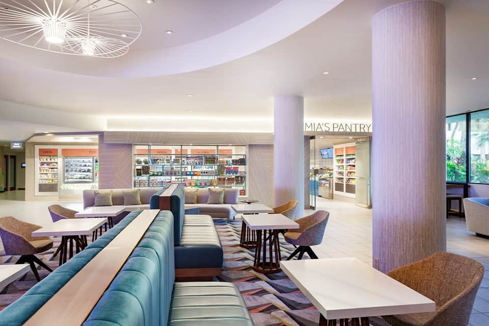 Modern hotel common area with blue seating, shops, and food pantry in contemporary clean design