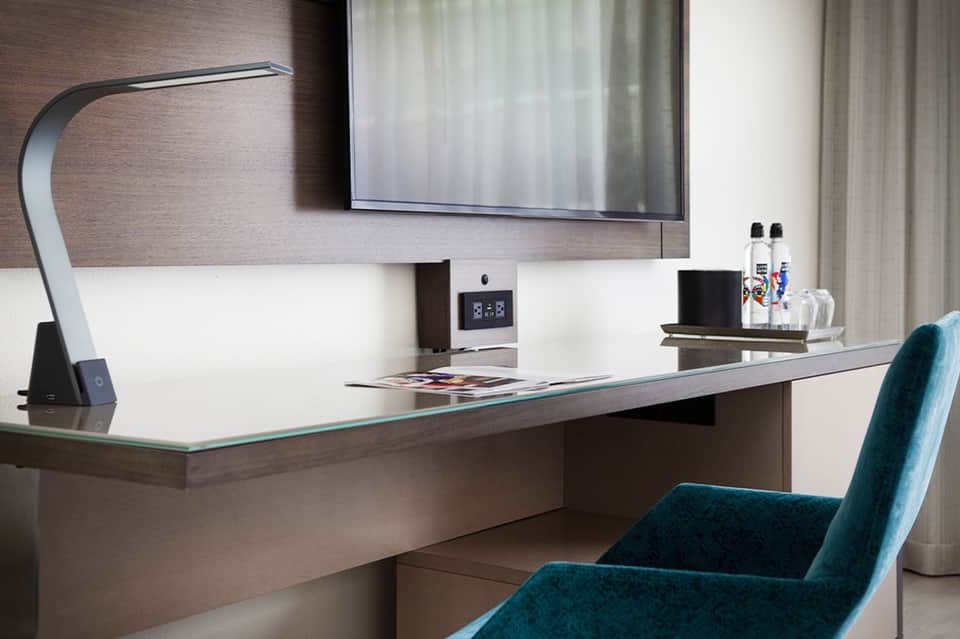 Modern hotel room desk with curved lamp, flat-screen TV, and contemporary furnishings