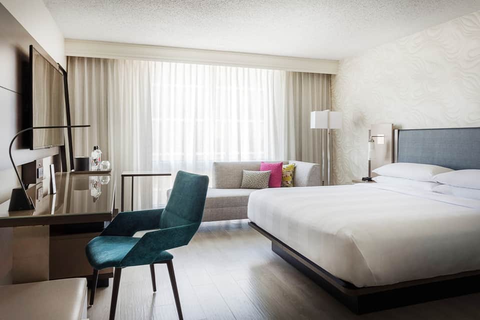 Contemporary hotel bedroom with king bed, teal accent chair, desk, flat-screen TV, and ocean view
