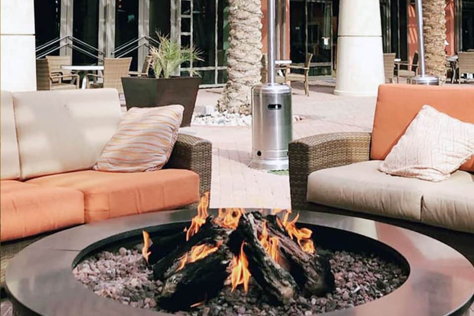 Outdoor patio with firepit, lounge seating in coral and cream, palm trees, and modern architecture