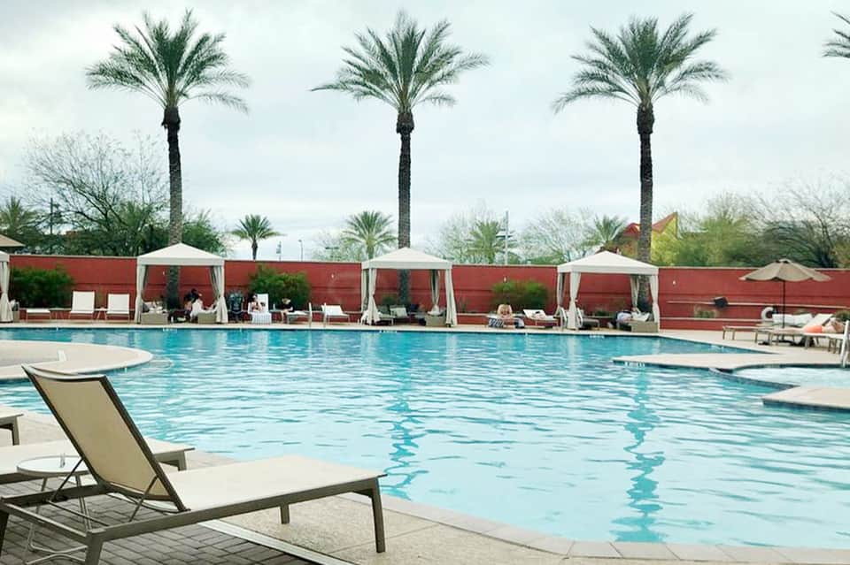 Resort pool with white cabanas, red privacy walls, and palm trees lining the deck