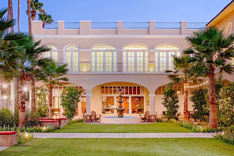 Elegant pink Mediterranean-style villa courtyard with arched colonnade and palm trees