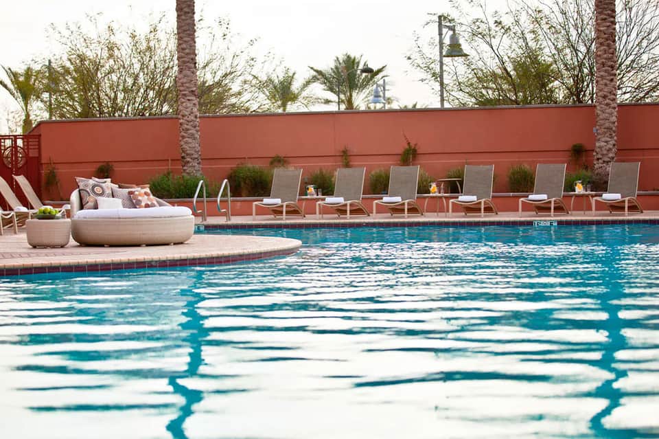 Resort pool with terracotta accent wall, lounge chairs, and palm trees in background