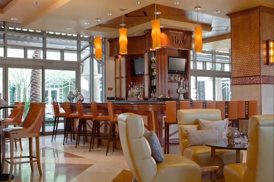 Upscale lounge bar with wood accents, orange pendant lights, views of palm trees, and contemporary seating