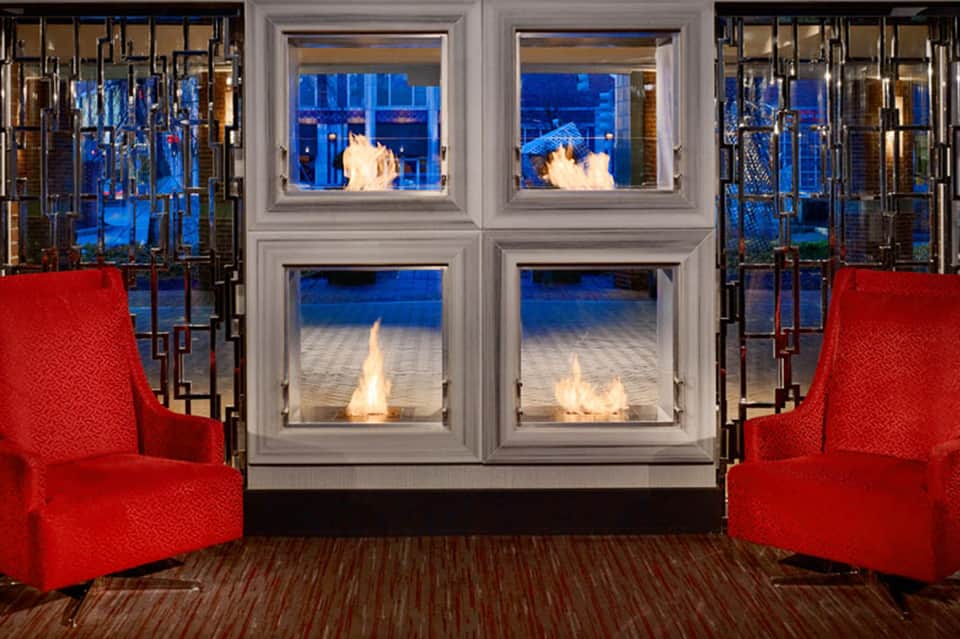 Modern fireplace with glass doors framed by red accent chairs and ocean views at dusk