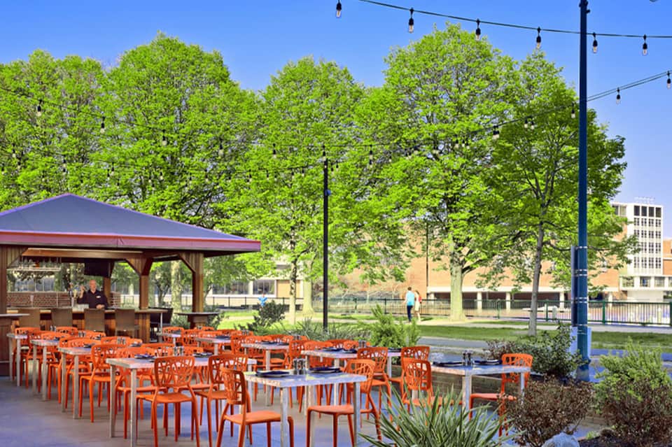 Outdoor patio with orange chairs, gazebo shelter, trees, and park setting