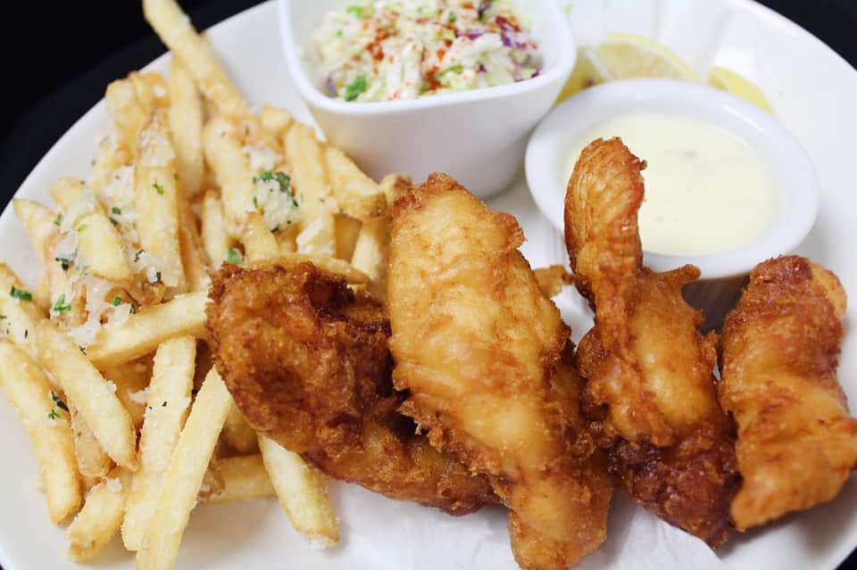 Plate of fried fish and chips with coleslaw and tartar sauce on white plate