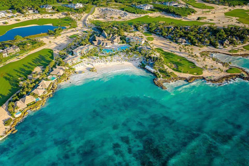 Aerial view of luxury beachfront resort with turquoise water, white sand beach, and manicured green grounds