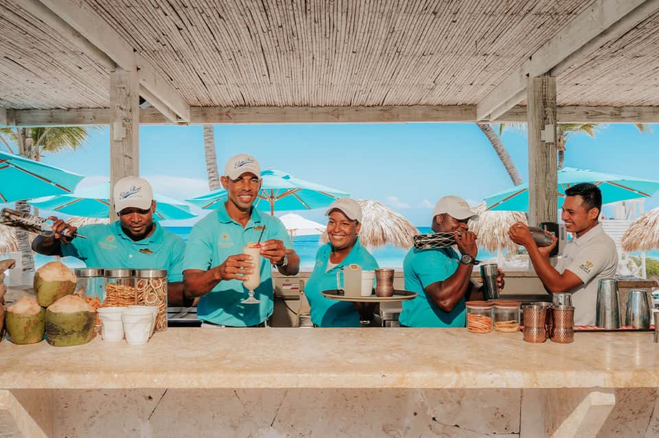 Beachside bar with staff in turquoise uniforms serving tropical drinks under thatched roof