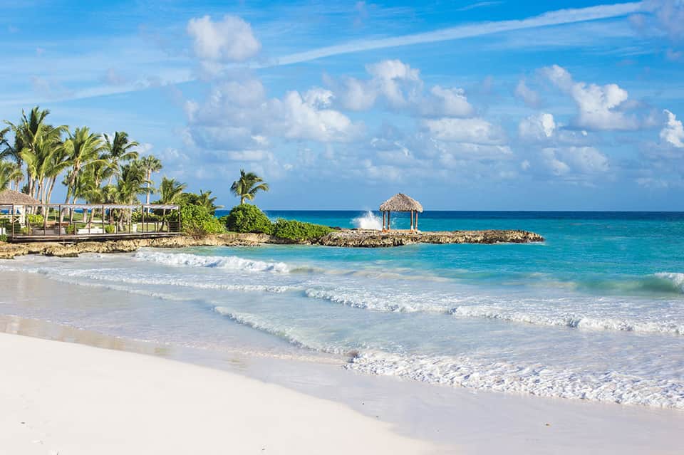 Beautiful white sand beach with turquoise ocean waves and tiki bar shelter among palm trees