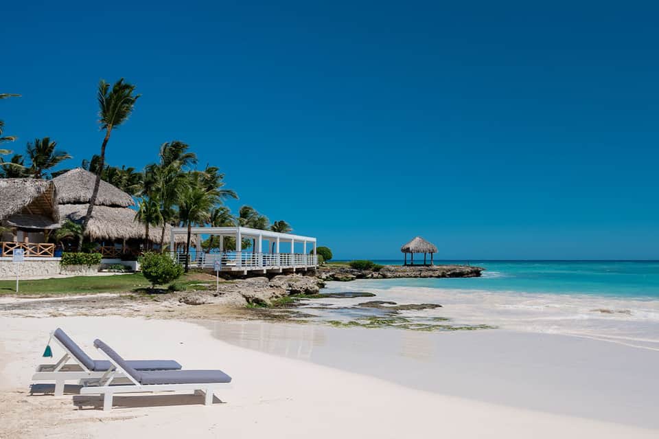 Luxury beachfront resort with thatched-roof structures, white lounge chairs, pristine turquoise water and palm trees
