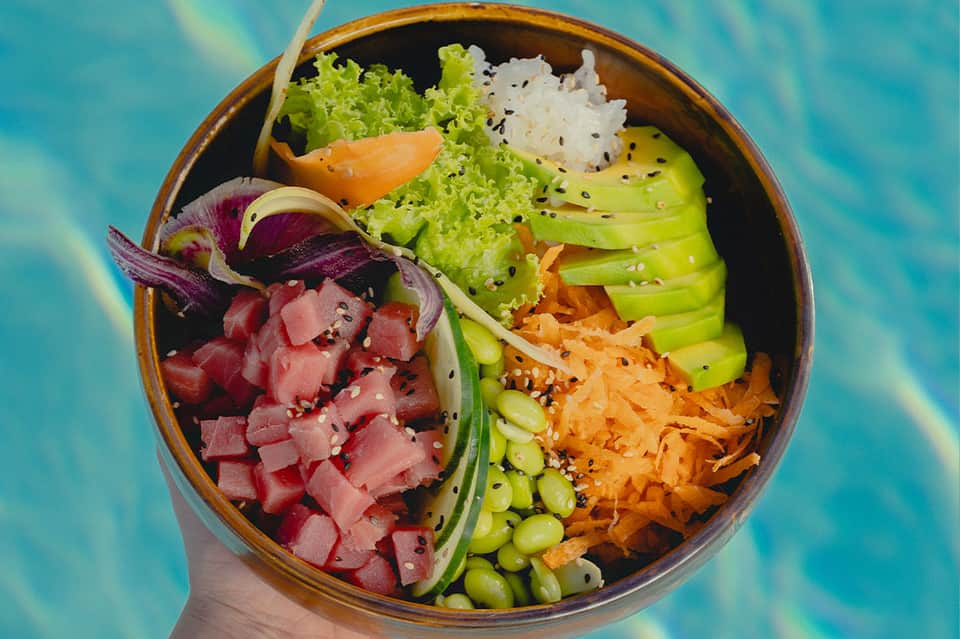 Colorful poke bowl with tuna, vegetables and rice by turquoise pool
