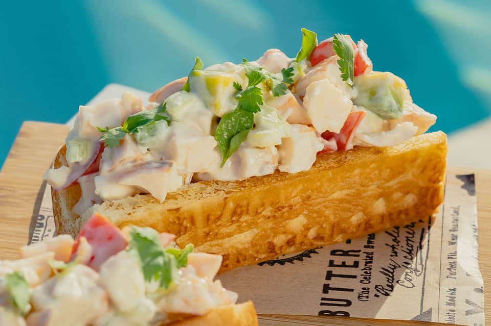 Gourmet lobster roll on toasted bread with fresh herbs and garnish against turquoise background