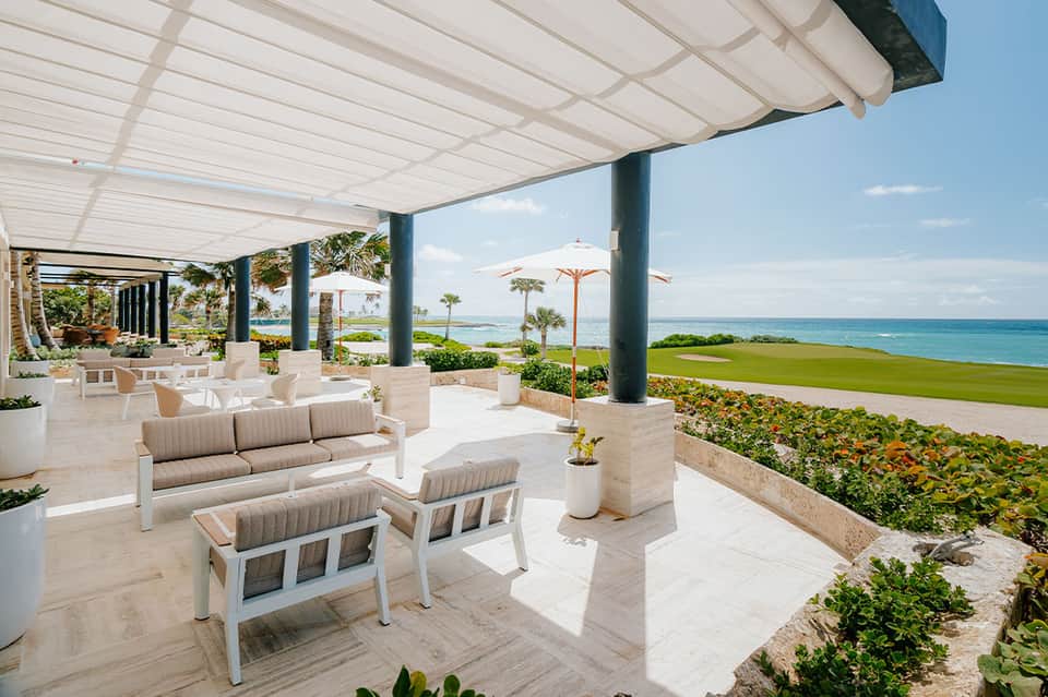 Beachfront terrace with modern lounge seating, white pergola, and ocean vista