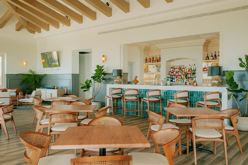 Contemporary hotel lounge with wooden beam ceiling, wooden chairs with rattan backs, teal tile accents, and full bar