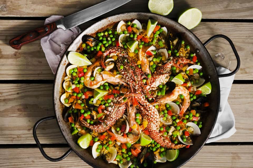 Paella dish with seafood and vegetables in large pan on wooden table