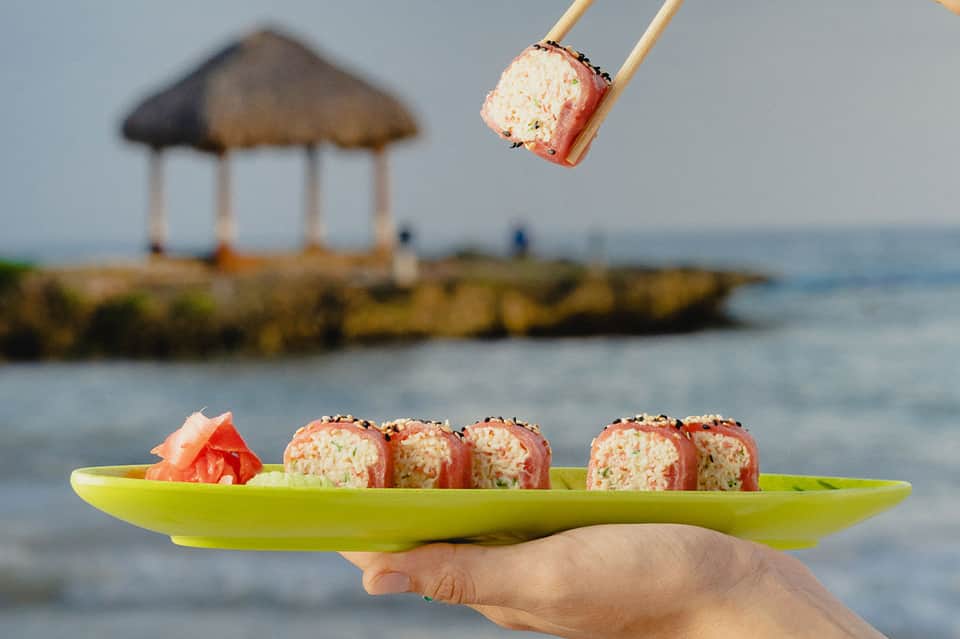 Sushi rolls on lime plate with beach gazebo and ocean in background