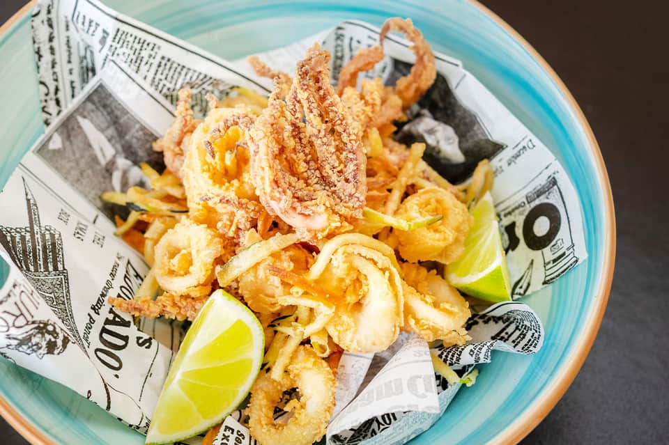 Plate of fried shrimp with lime wedges on newspaper-lined turquoise plate