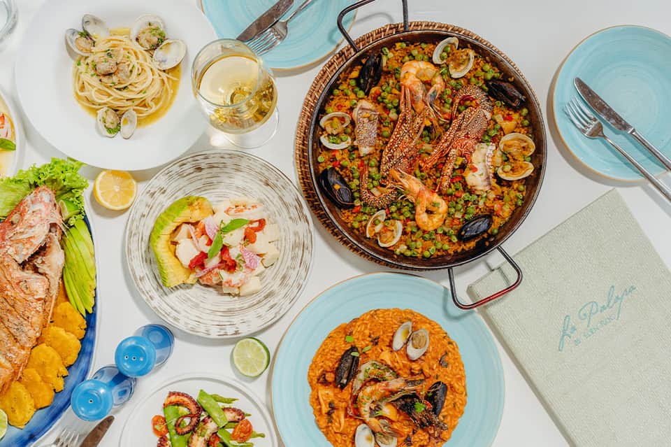 Overhead view of Spanish seafood paella and various Mediterranean dishes with white wine